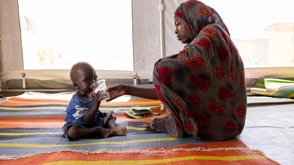 Eine Mutter gibt ihrem Kind einen Becher mit Flüssigkeit
