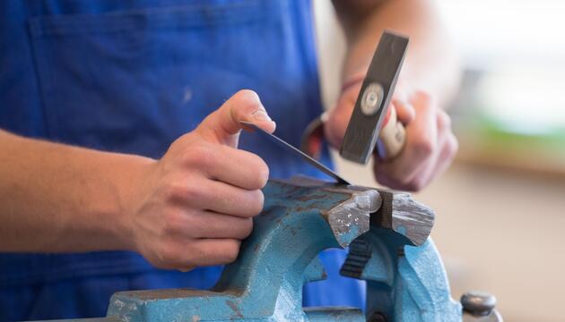 Auszubildender steht mit einem Hammer an einem Schraubstock