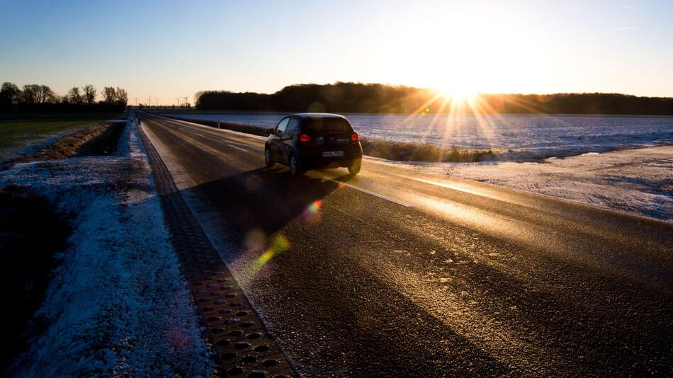 Auto fährt bei Sonnenaufgang über eine spiegelglatte Landstrasse