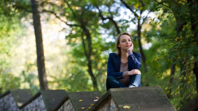 Eine Frau sitzt nachdenklich auf einer Mauer im Park