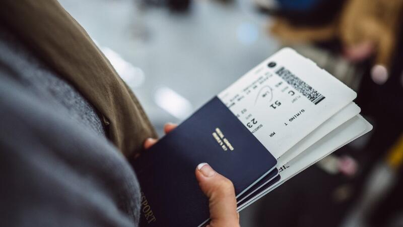 Ein Fluggast hält seinen Reisepass und Flugtickets in der Hand.