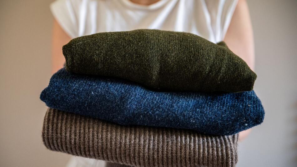 Eine Frau hält einen Stapel Woll-Pullover