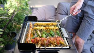 Ein Mann grillt mit einem Elektrogrill auf einem Balkon