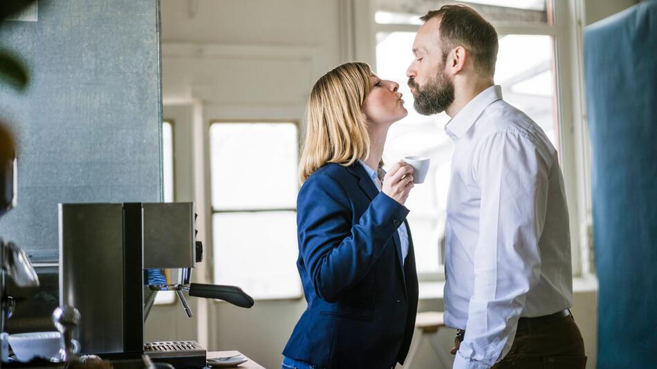 Zwei Personen küssen sich in einem Büro