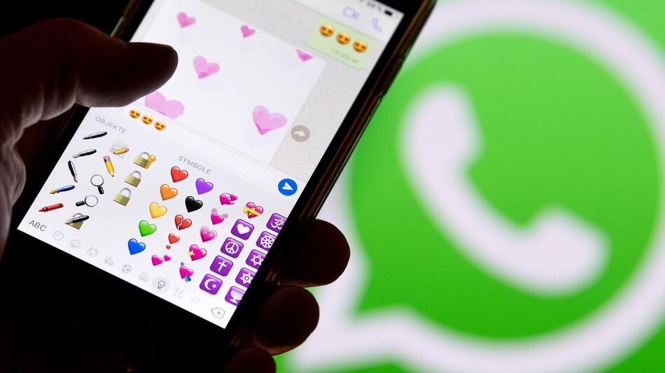 Smartphone mit Emojis aus WhatsApp vor dem WhatsApp-Logo