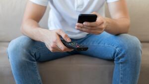 Mann mit Fernbedienung und Smartphone in der Hand