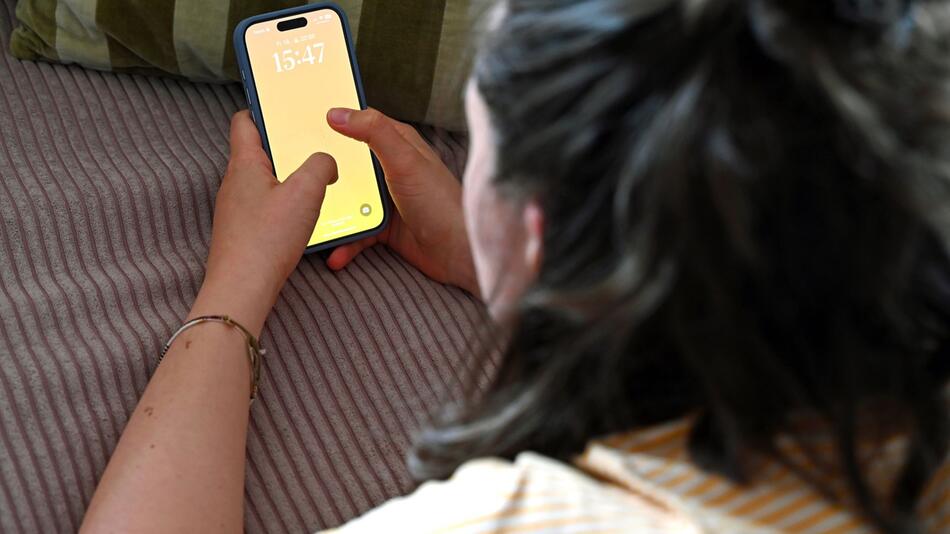 Frau liegt auf dem Sofa und schaut auf ein Smartphone