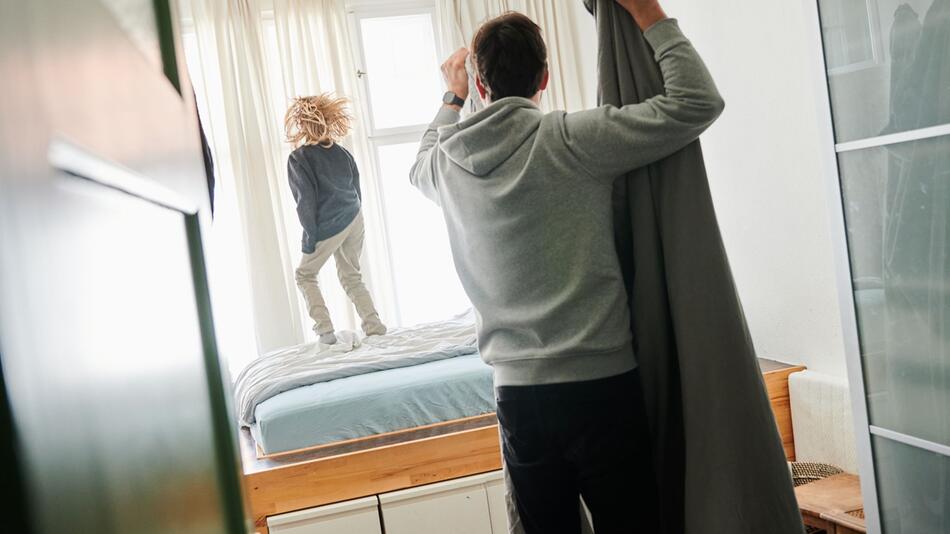 Mann bezieht ein Bett während ein Kind auf dem Bett hüpft