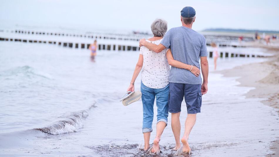 Ein Rentner-Paar spaziert am Strand entlang