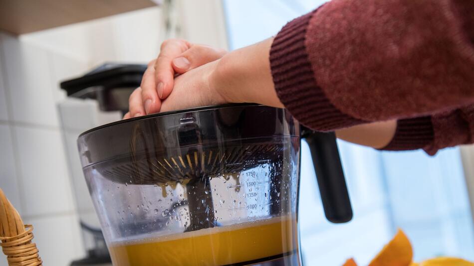 Mann macht mit einem Entsafter frischen Orangensaft