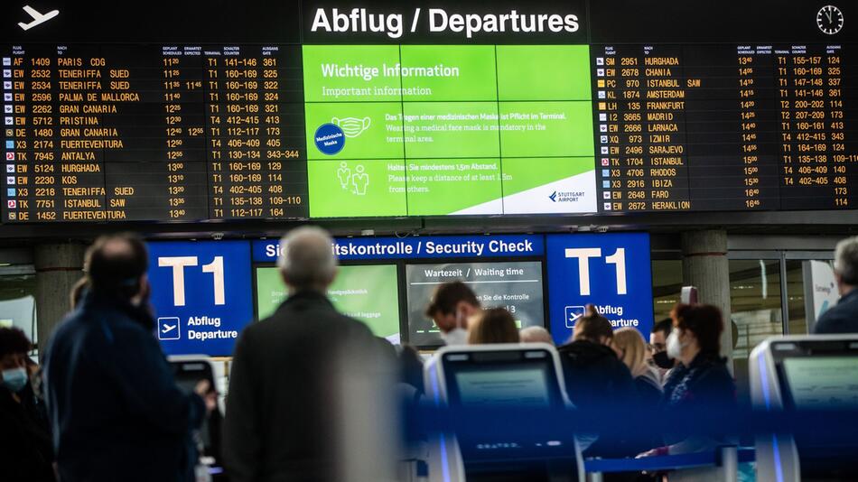 Urlauber stehen vor einer Anzeigetafel am Flughafen