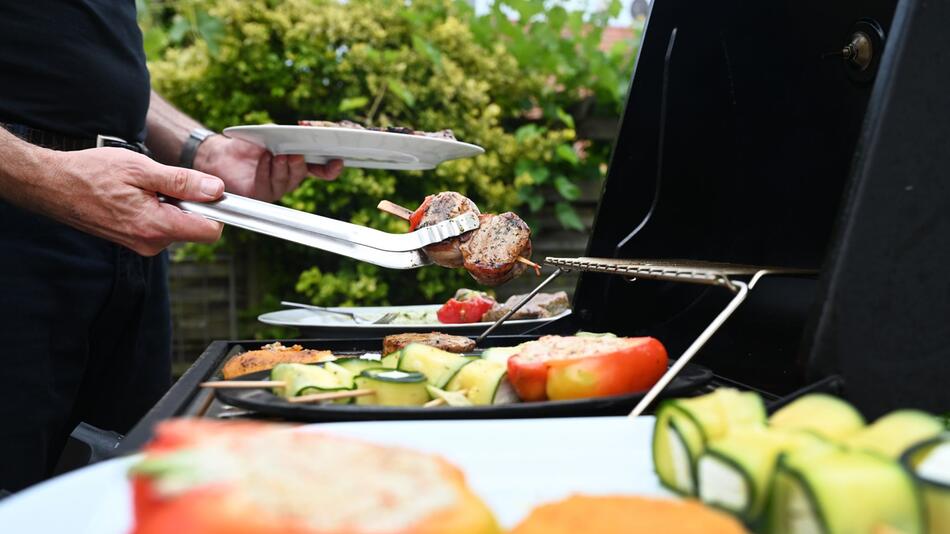 Eine Mann wendet mit einer Zange Grillfleisch auf einem Gasgrill