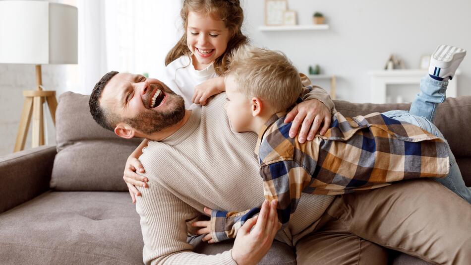 Vater tobt mit zwei Kindern auf dem Sofa
