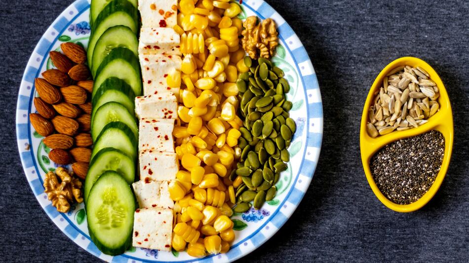 Ein Teller mit in Reihen angeordneten Mandeln, Gurkenscheiben, gewürztem Tofu, Maiskörnern ...