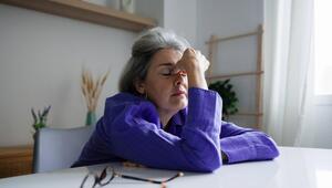 Eine Frau sitzt erschöpft an einem Tisch und fasst sich an die Stirn.