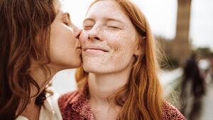 Junge Frau küsst ebenfalls junge Frau mit Sommersprossen auf die Wange