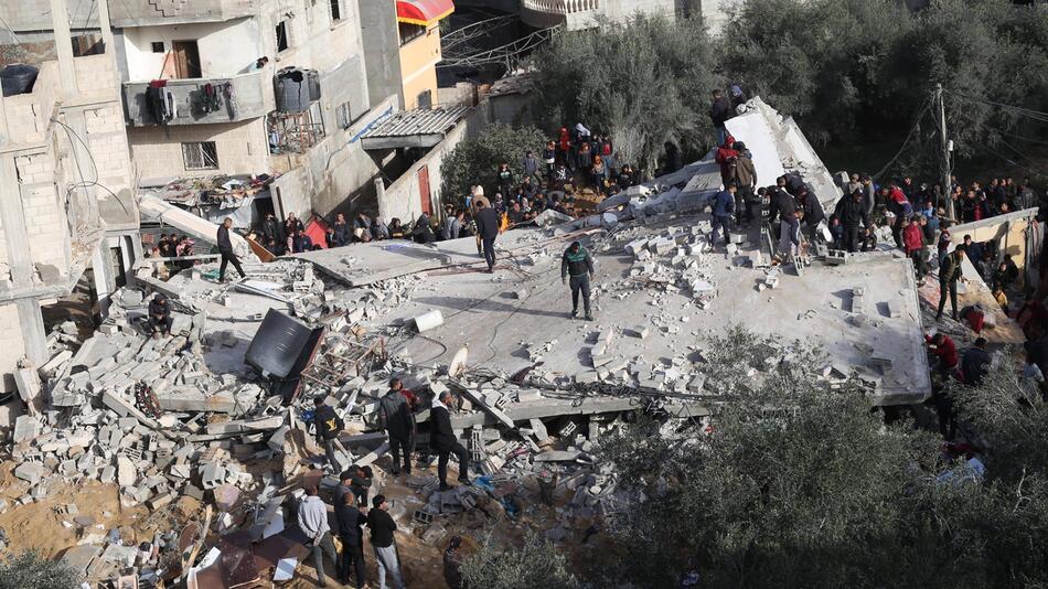 Menschen stehen auf einem zerstörten Gebäude in der Stadt Rafah.