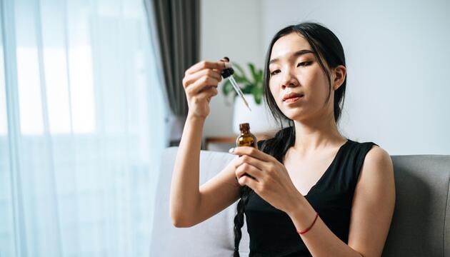 Junge Frau mit schwarzen Haaren, die eine Pipette in der Hand hält. 