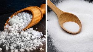 Links grobkörniges Meersalz in einem Holzlöffel auf dunklem Untergrund, rechts feinkörniges ...