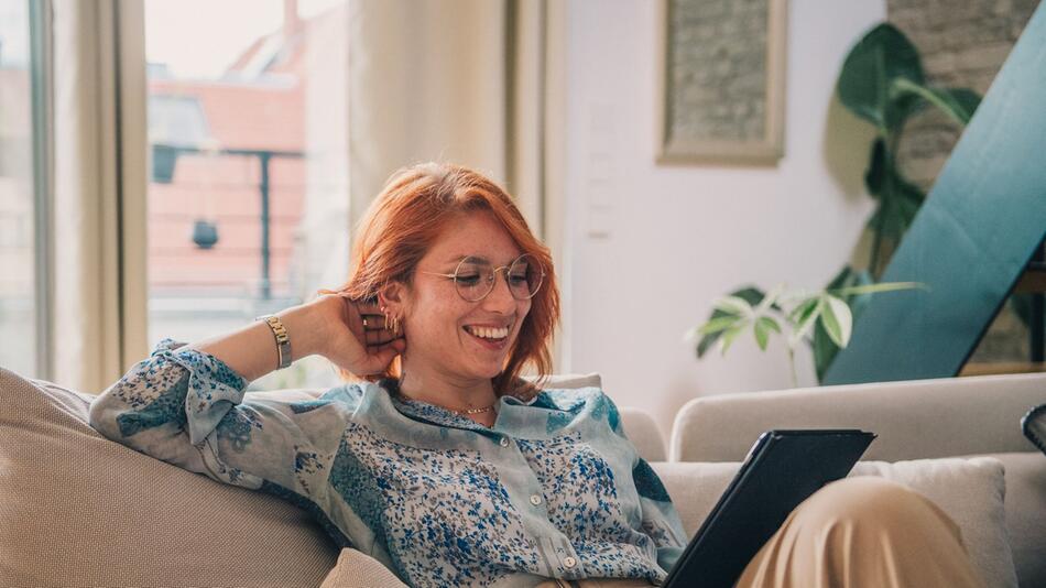 Eine Frau sitzt auf einer Couch und bedient ein Tablet