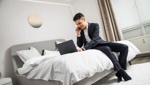 Ein Mann im Anzug sitzt auf einem Bett und arbeitet am Laptop