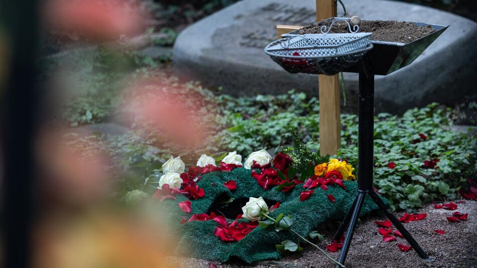 Frisches Urnengrab mit Holzkreuz und Blumen