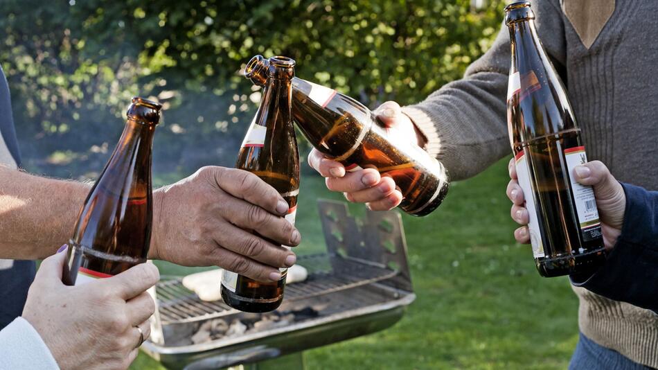 Vier Leute stossen draussen vor einem Grill mit Bierflaschen an