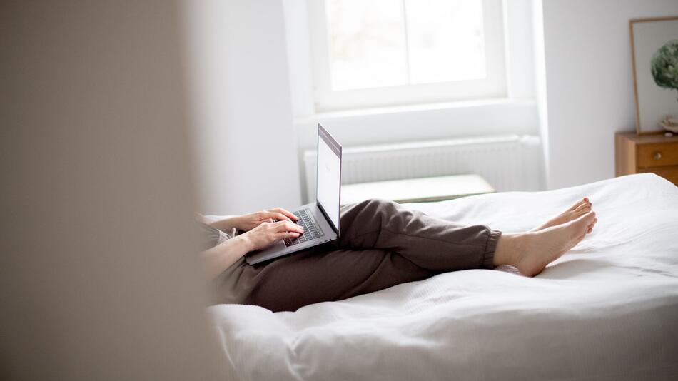 Eine Frau sitzt mit Laptop auf einem Bett