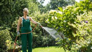 Eine Frau giesst Pflanzen mit einem Gartenschlauch