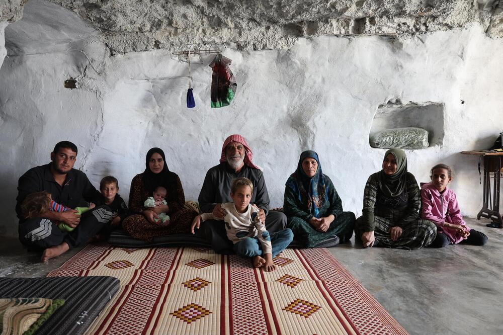 Fünf Erwachsene und mehrere Kinder sitzen vor einer weissen Wand in einer Höhle.