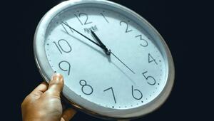 Hand hält eine runde Wanduhr mit weissem Zifferblatt und schwarzen Zahlen, die Uhrzeit zeigt 11 ...
