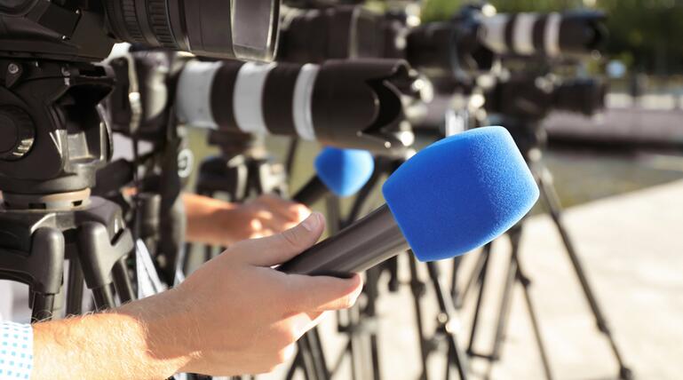 Journalists with microphones and video cameras outdoors, closeup
