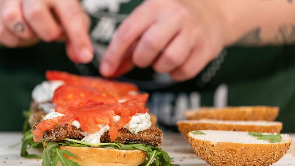 Eine Köchin belegt einen Burger mit veganem Fischersatz