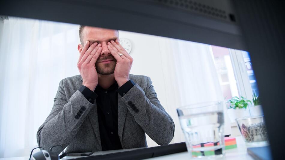 Ein Mann reibt sich die Augen am Schreibtisch