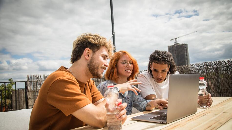 Junge Leute sitzen auf einer Dachterrasse vor einem Laptop