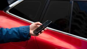 Mann steht mit seinem Smartphone vor einem Auto