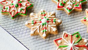 Mehrere sternförmige Weihnachtsplätzchen auf einem Metallgitter, verziert mit weissem, rotem und ...
