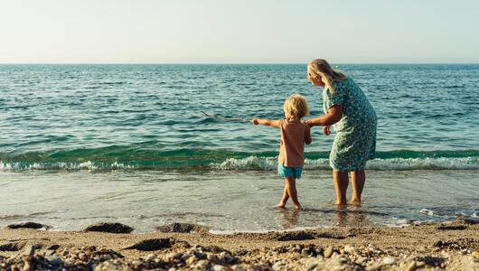 Ältere Frau und Kind schauen vom Strand aus aufs Meer