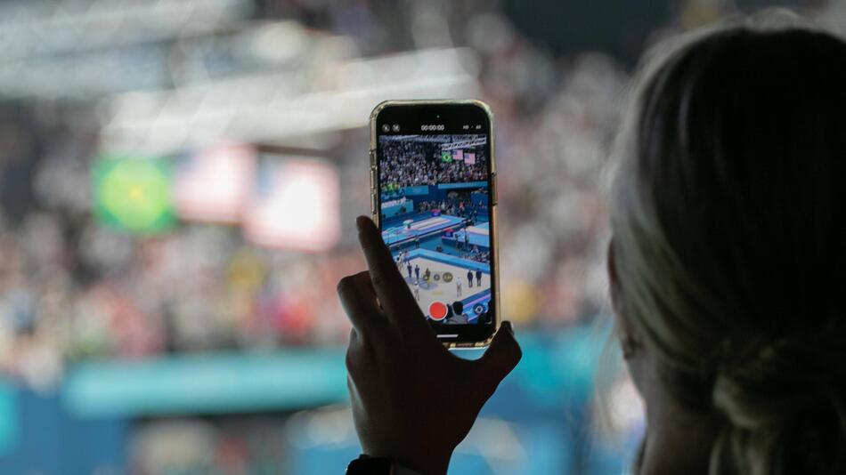 Ein weiblicher Fan filmt die Siegerehrung im Turnen der Frauen von der Tribüne aus mit