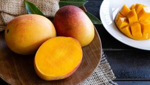 Drei Mangos auf Holztablett. Eine Hälfte wird in Würfel geschnitten. 