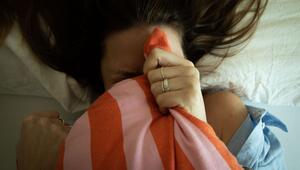 Frau versteckt sich hinter einem Kissen