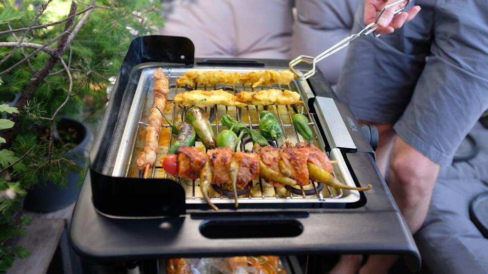 Ein Mann grillt mit einem Elektrogrill auf einem Balkon