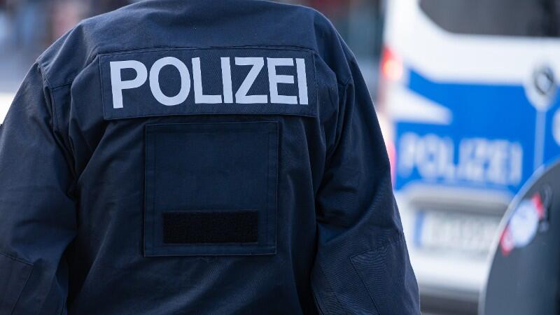 Ein Polizist mit seiner Uniform steht vor einem Polizeiwagen.