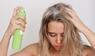 Junge blonde Frau mit schmutzigem, fettigem Haar, die ein Trockenshampoo auf die Haarwurzeln sprüht