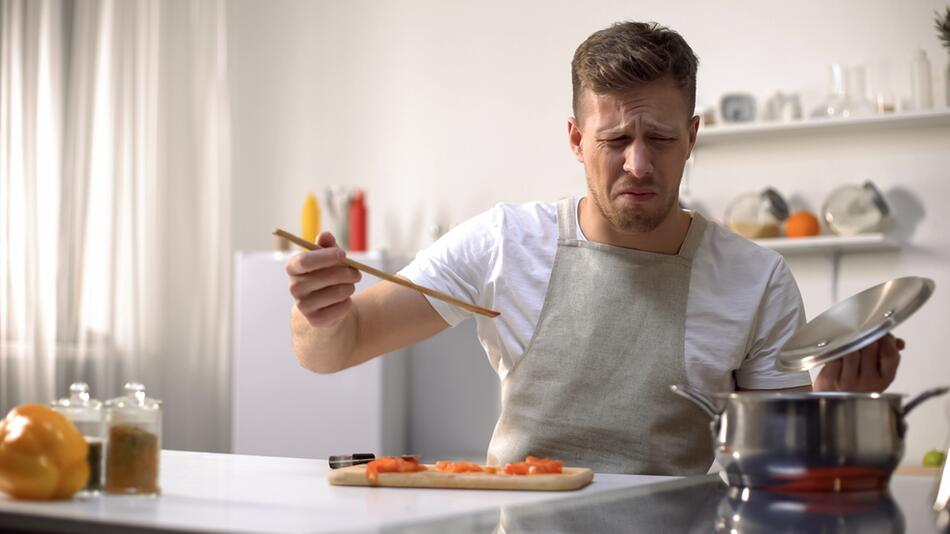 Mann verzieht das Gesicht beim Kochen