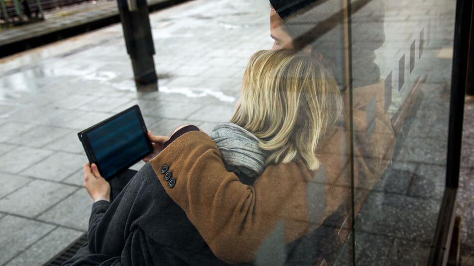 Ein Paar sieht auf ein Tablet am Bahnhof