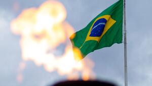 Brasilianische Flagge an einem Fahnenmast vor bewölktem Himmel, im Vordergrund unscharfe Flammen.