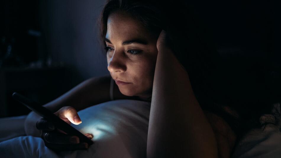 Frau legt im Bett und schaut auf ihr Handy