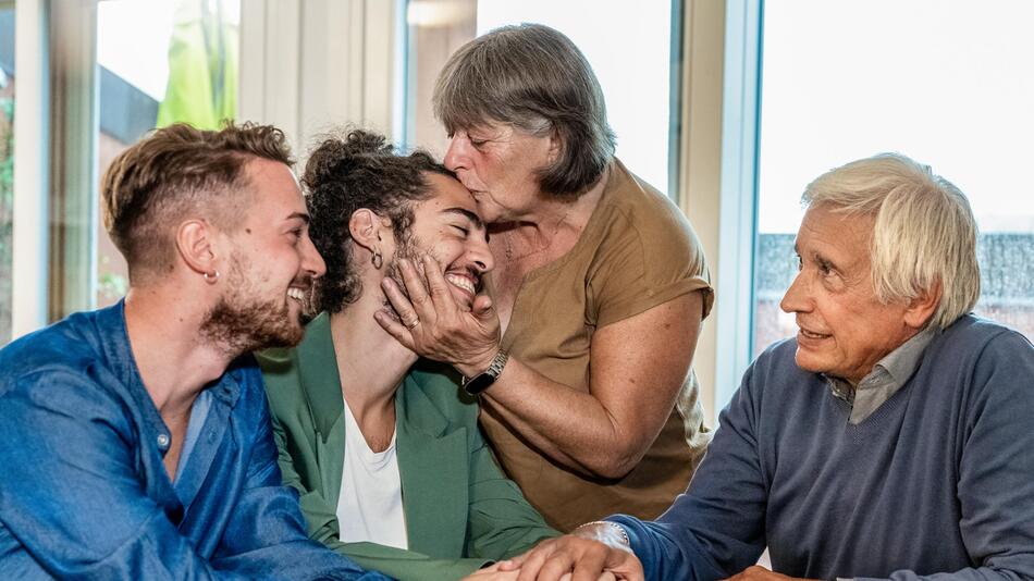 Queeres Paar outet sich vor Grosseltern, die mit Umarmungen und Küssen reagieren.