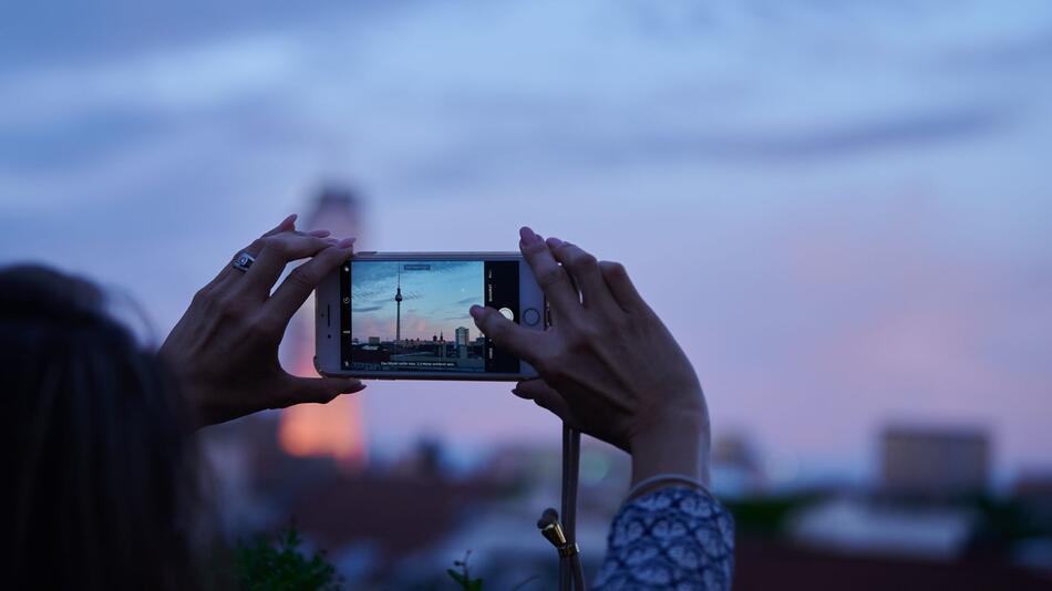 Frau fotografiert mit dem Smartphone den Abendhimmel über Berlin